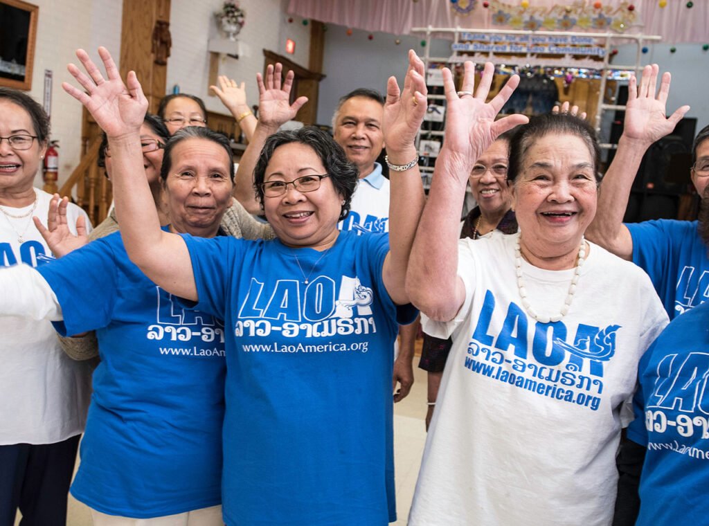Laotian-American seniors wearing LaoAmerica.org t-shirts smiling and waving.