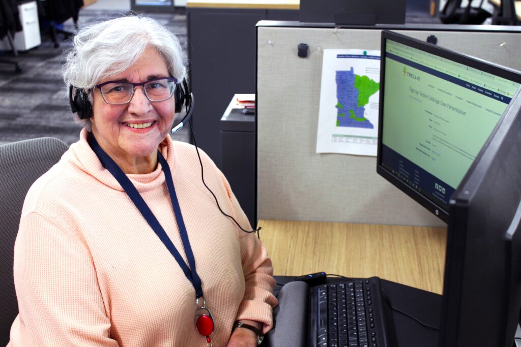 woman at computer with headset smiling at camera